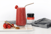 Red berry smoothie next to a UMF 15+ MGO 514+ Manuka honey jar with strawberries
