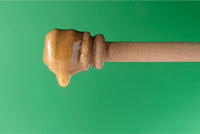 Honey dripping from a wooden dipper against a green background, UMF 28+ MGO 1450+ Manuka honey