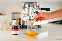Espresso machine pouring into a yellow cup beside a UMF 15+ MGO 514+ Manuka honey jar