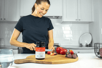 Woman in a kitchen with chopping board, fruit and a UMF 15+ MGO 514+ Manuka honey jar