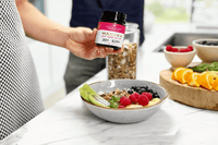 Hand holding UMF 20+ MGO 829+ Manuka honey jar over a yoghurt bowl with berries