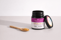 Open UMF 24+ MGO 1122+ Manuka honey jar with bamboo spoon and lid placed beside it