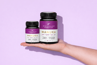 Two UMF 24+ MGO 1122+ Manuka honey jars in different sizes held in a hand on lavender