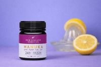 UMF 24+ MGO 1122+ Manuka honey jar on purple surface with fresh lemon and a juicer