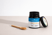 Open UMF 26+ MGO 1282+ Manuka honey jar with bamboo spoon and lid placed beside it