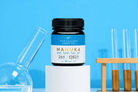 UMF 26+ MGO 1282+ Manuka honey jar on a pedestal with science lab glassware on blue