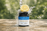 Water splashing around a UMF 26+ MGO 1282+ Manuka honey jar with a lemon slice on top