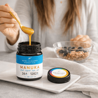 Hand lifting honey with a wooden spoon from an open UMF 26+ MGO 1282+ Manuka honey jar