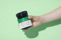 Hand holding a UMF 28+ MGO 1450+ Manuka honey jar against a green background