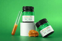 Two UMF 28+ MGO 1450+ Manuka honey jars styled on a green background with honeycomb