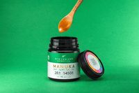 Bamboo spoon lifting honey out of an open UMF 28+ MGO 1450+ Manuka honey jar on green