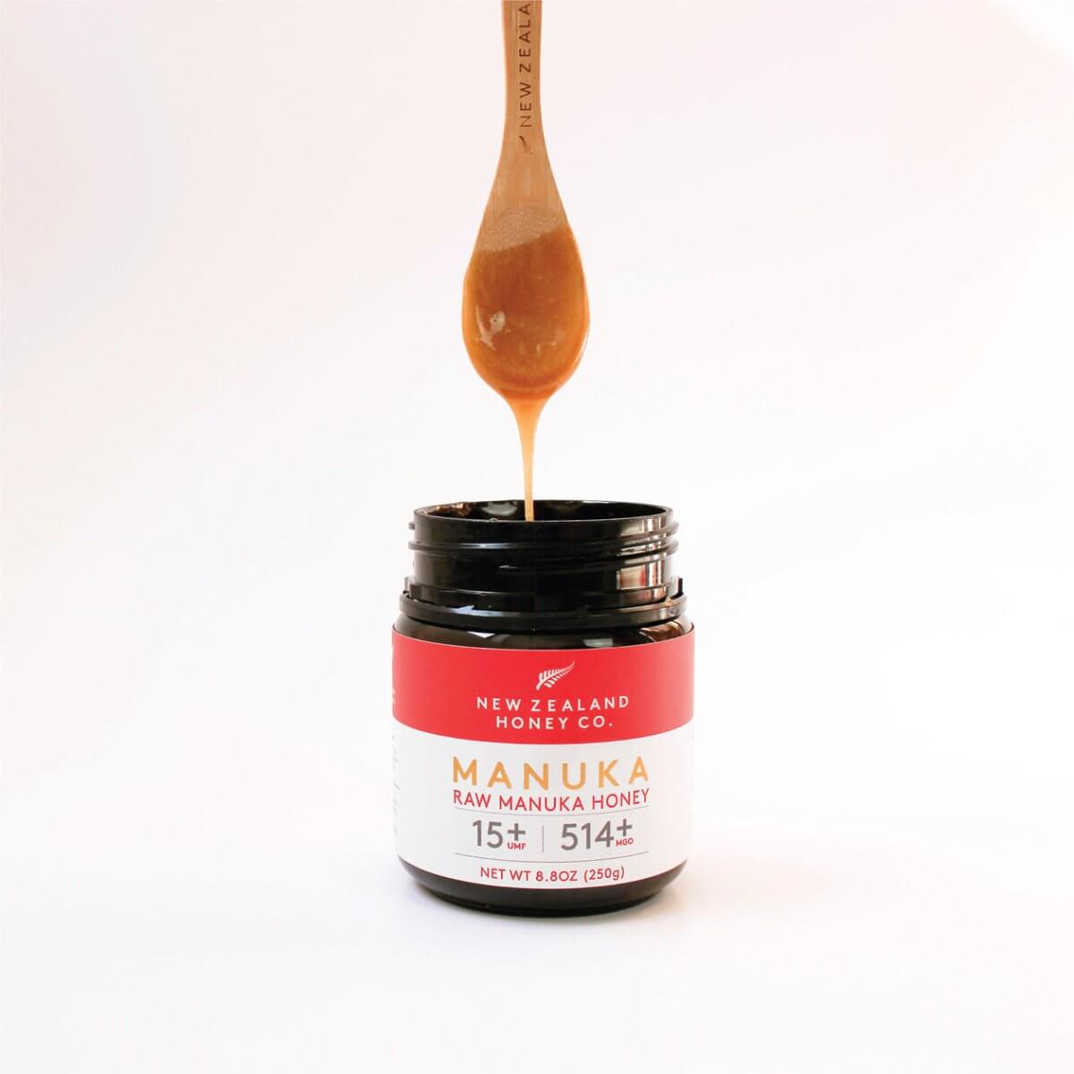 Wooden honey spoon drizzling honey into a UMF 15+ Manuka honey jar