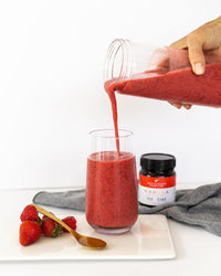 Pouring red berry smoothie into a glass beside a UMF 15+ MGO 514+ Manuka honey jar