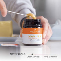 Close-up of a hand dipping a stick into an open UMF 10+ MGO 263+ Manuka honey jar