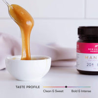 Honey dripping from a spoon into a white bowl with UMF 20+ MGO 829+ Manuka honey jar behind